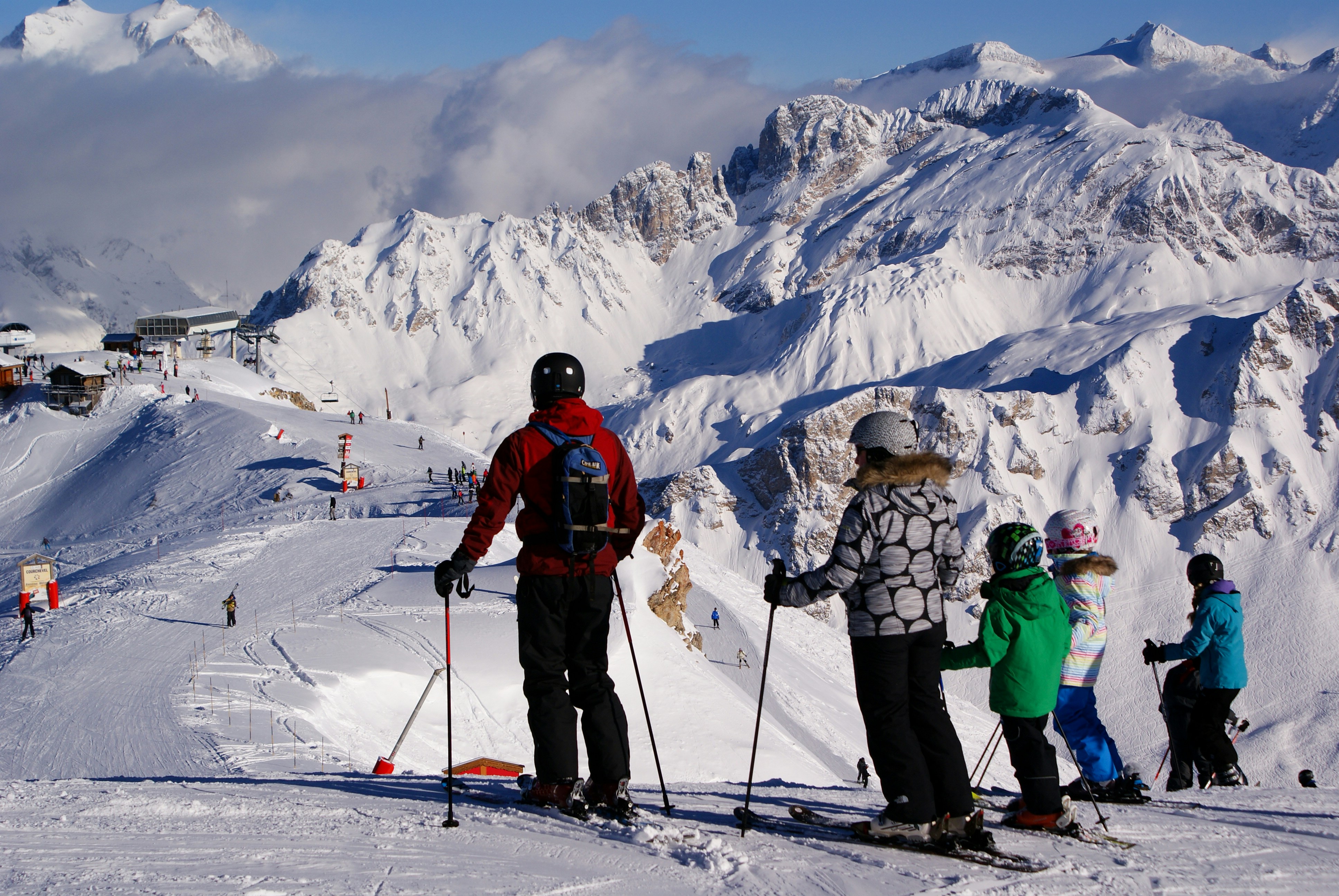 Family group of skiers on a wide alpine slope overlooking snowy peaks in the French Alps